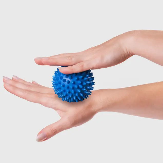 Frauenhände rollen Massageball über den Handrücken.