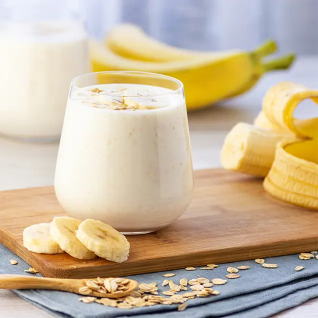 Bananensmoothie auf Holzbrett mit frischen Bananen im Hintergrund.