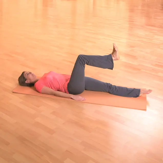 Frau liegt auf dem Rücken auf einer Yogamatte und winkelt ein Bein an.