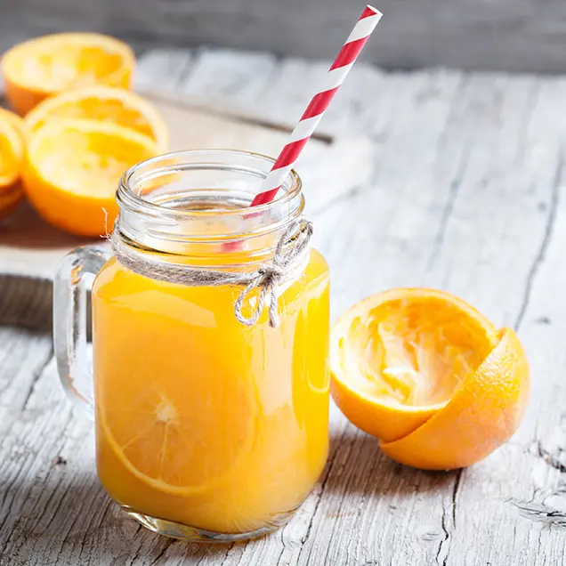 Glas mit frisch gepresstem Orangensaft und Strohhalm.