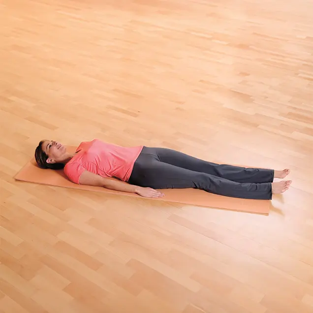 Frau liegt ausgestreckt auf dem Rücken auf einer Yogamatte.