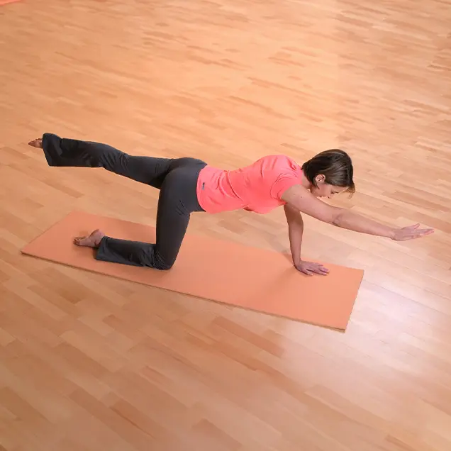 Frau kniet auf einer Yogamatte im Vierfüßlerstand und streckt einen Arm und ein Bein aus.