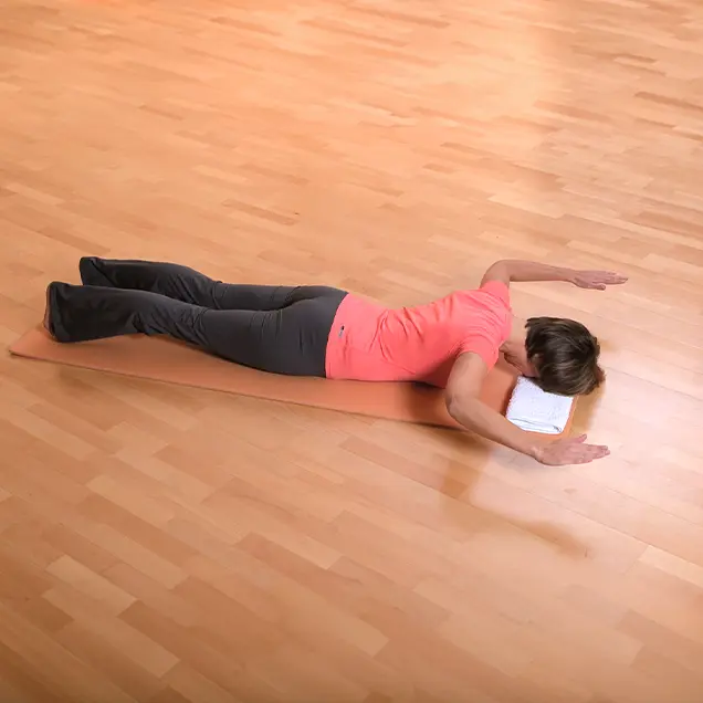 Frau liegt auf dem Bauch auf einer Yogamatte und hebt die Arme an.