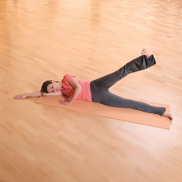 Frau liegt ausgestreckt auf der Seite auf einer Yogamatte und streckt ein Bein nach oben.