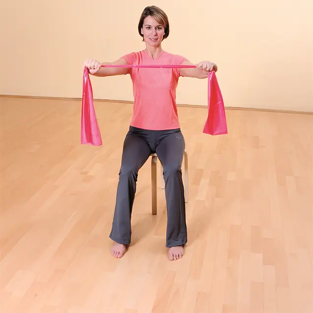 Frau sitzt auf einem Hocker und hält ein Fitnessband in den Händen.