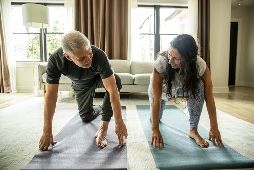 Mann und Frau beim Yoga im Wohnzimmer.